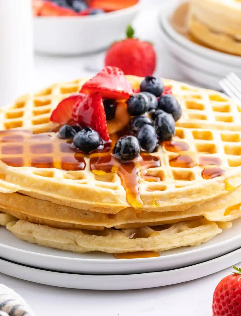 A golden-brown waffle with melting butter, served with fresh berries and syrup on a white plate