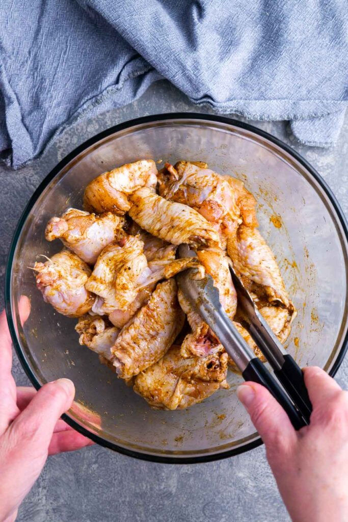 A bowl of chicken wings being tossed in seasonings, with a hand mixing them thoroughly.