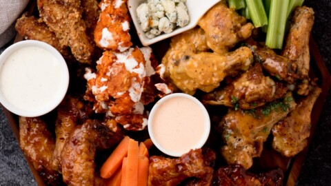 A serving platter with a variety of dips like ranch, blue cheese, and BBQ sauce, surrounded by chicken wings, celery, and carrot sticks.