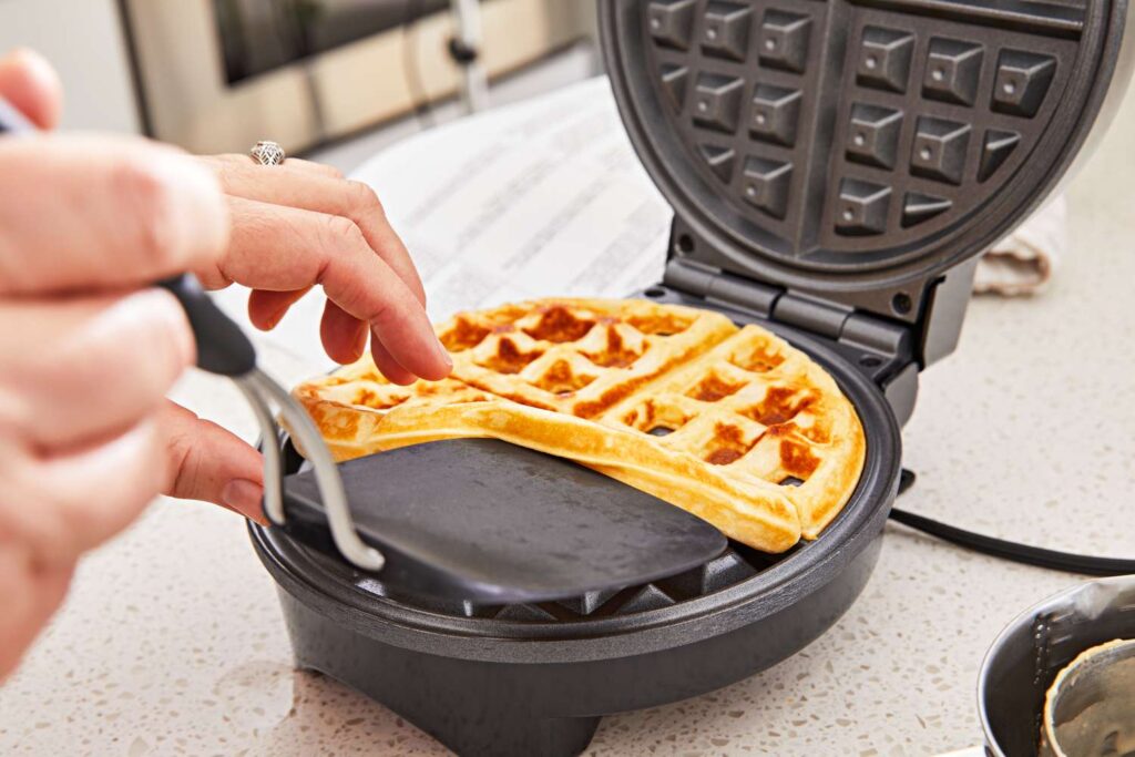 A golden-brown waffle being lifted effortlessly from a waffle iron with a non-stick surface.