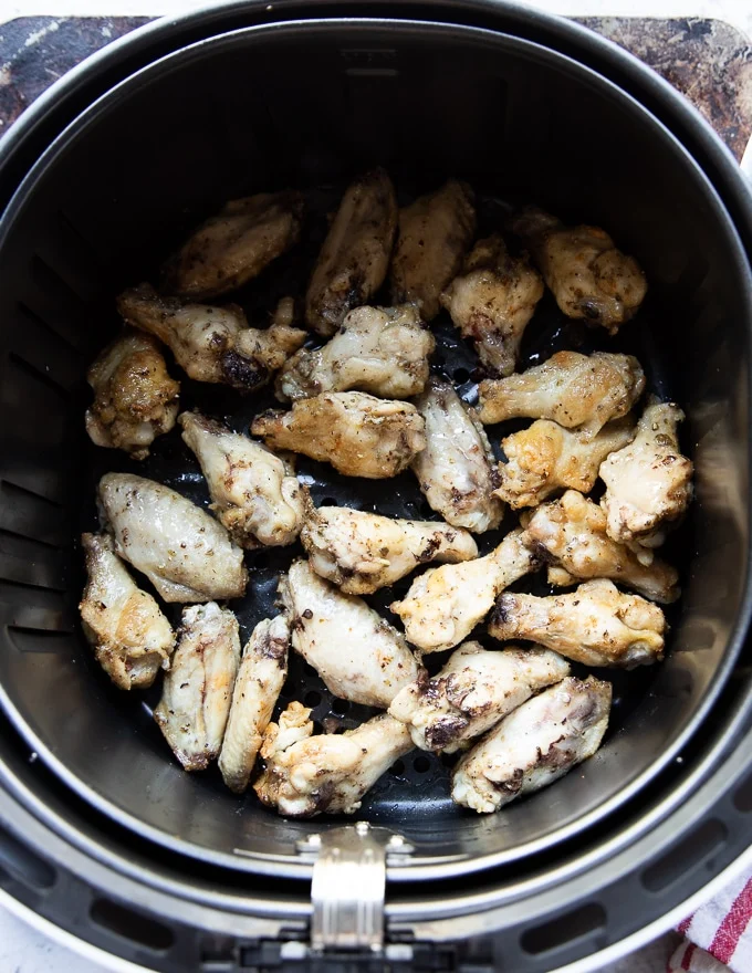 A shot of chicken wings arranged in a single layer in an air fryer basket, ready to be cooked.