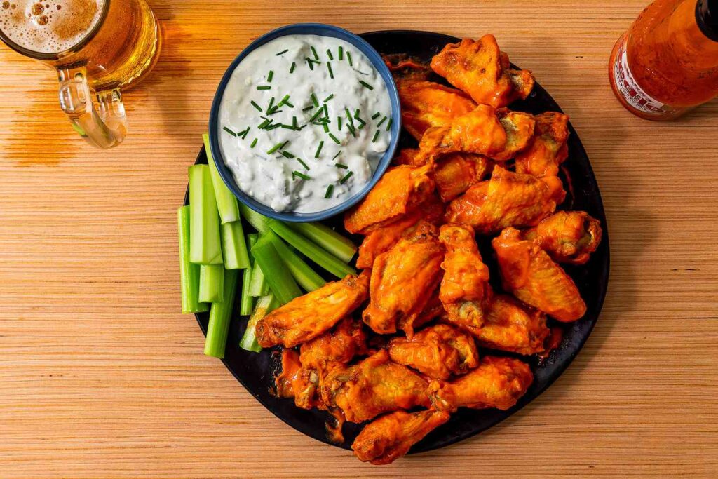 A plate of classic Buffalo wings, coated in a vibrant, spicy sauce and served with celery sticks and cheese dressing.