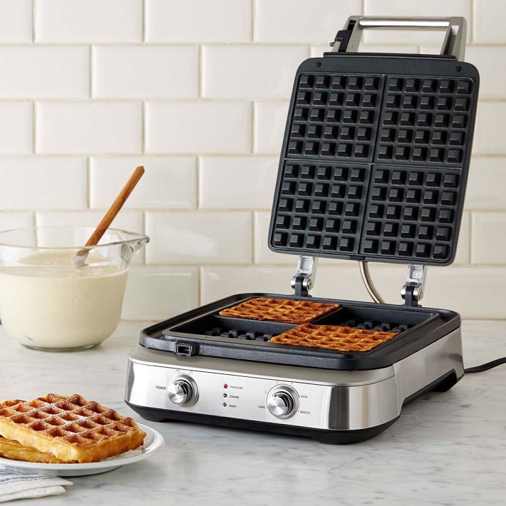 A Breville Smart Waffle Pro waffle maker on a kitchen counter, with a stack of four golden-brown waffles next to it.