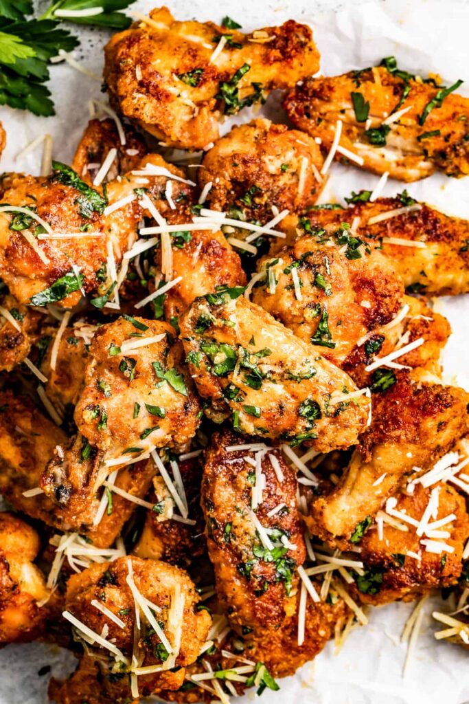 A plate of garlic Parmesan wings, sprinkled with extra Parmesan cheese and chopped parsley.