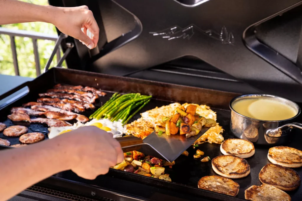 An indoor grill and griddle with steaks, vegetables, and pancakes cooking on it.