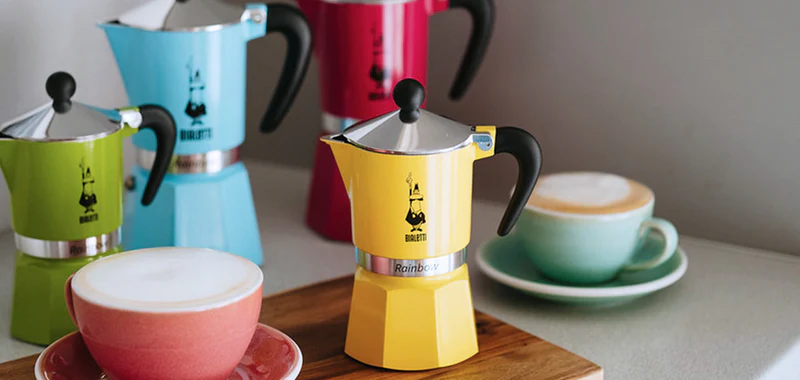 Classic Bialetti Moka Pot brewing coffee on a stovetop, showing steam rising from the spout and rich coffee filling the upper chamber."